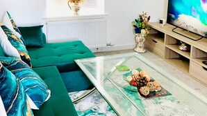Een moderne woonkamer met een groene bank, een glazen salontafel en een televisie op een houten dressoir.