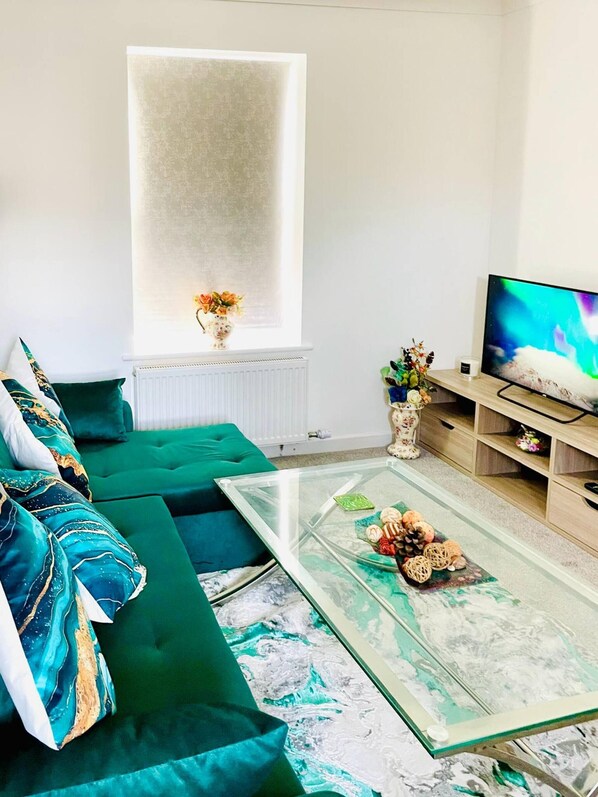En moderne stue med en grøn sofa, et glasbord og et fjernsyn på et træstel.