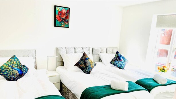 Een hotelkamer met twee bedden, witte beddengoed, blauwgroene plaids en decoratieve kussens met pauwendesigns.