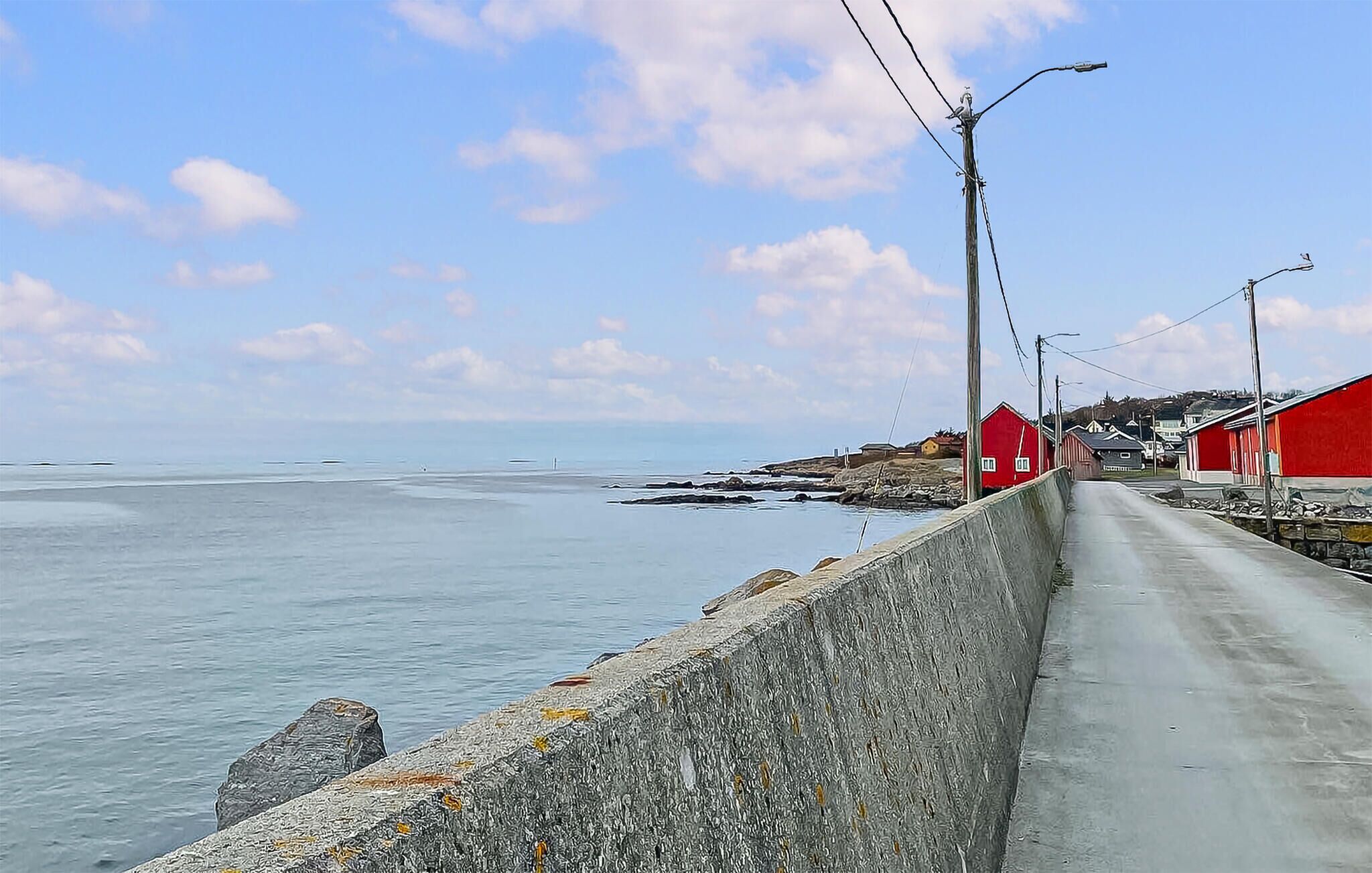 A coastal road with a concrete barrier, a red building, and a clear sky.