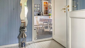A narrow hallway with a door leading to a dining area. The hallway has a blue wall and a white door with brass handles. There is a metal lantern on the floor and a table with chairs in the dining area. - 3 bedroom cozy apartment in Myklebost (Myklebost)