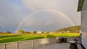 A deck with a view of a rainbow over a green field and houses. - 3 bedroom cozy apartment in Myklebost (Myklebost)