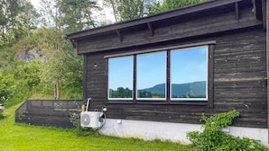 A wooden cabin with a large window, a small air conditioning unit, and a grassy yard. - Amazing apartment in Kvisvik (Kvisvik)