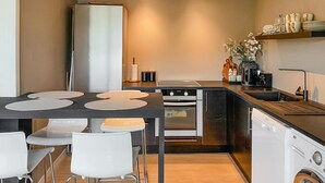A compact kitchen with a refrigerator, stove, oven, and dishwasher. There are two white chairs and a table with placemats. A sink and a vase with flowers are also visible. - Amazing apartment in Kvisvik (Kvisvik)