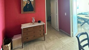 Een kamer met een rode muur, een houten dressoir, een lijst met een schilderij en een deur naar een andere kamer.