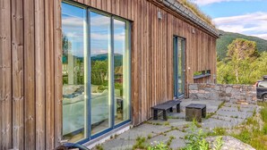 A wooden cabin with large sliding glass doors, a stone wall, and a stone bench.