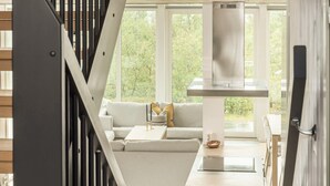 A modern interior with a staircase, a sofa, a dining table, and a kitchen area with a range hood.