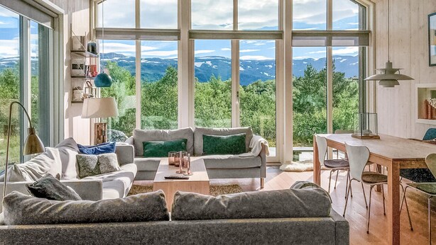 A spacious living room with a large window offering a mountain view, a cozy sofa, a dining area, and a lamp.