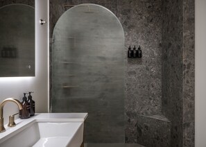 Une salle de bain moderne avec un grand miroir, un lavabo blanc et une douche dotée d’une porte en verre.