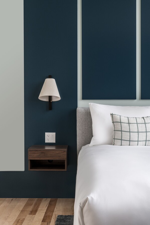 Un dormitorio con cama, mesita de noche, lámpara y enchufe en la pared.