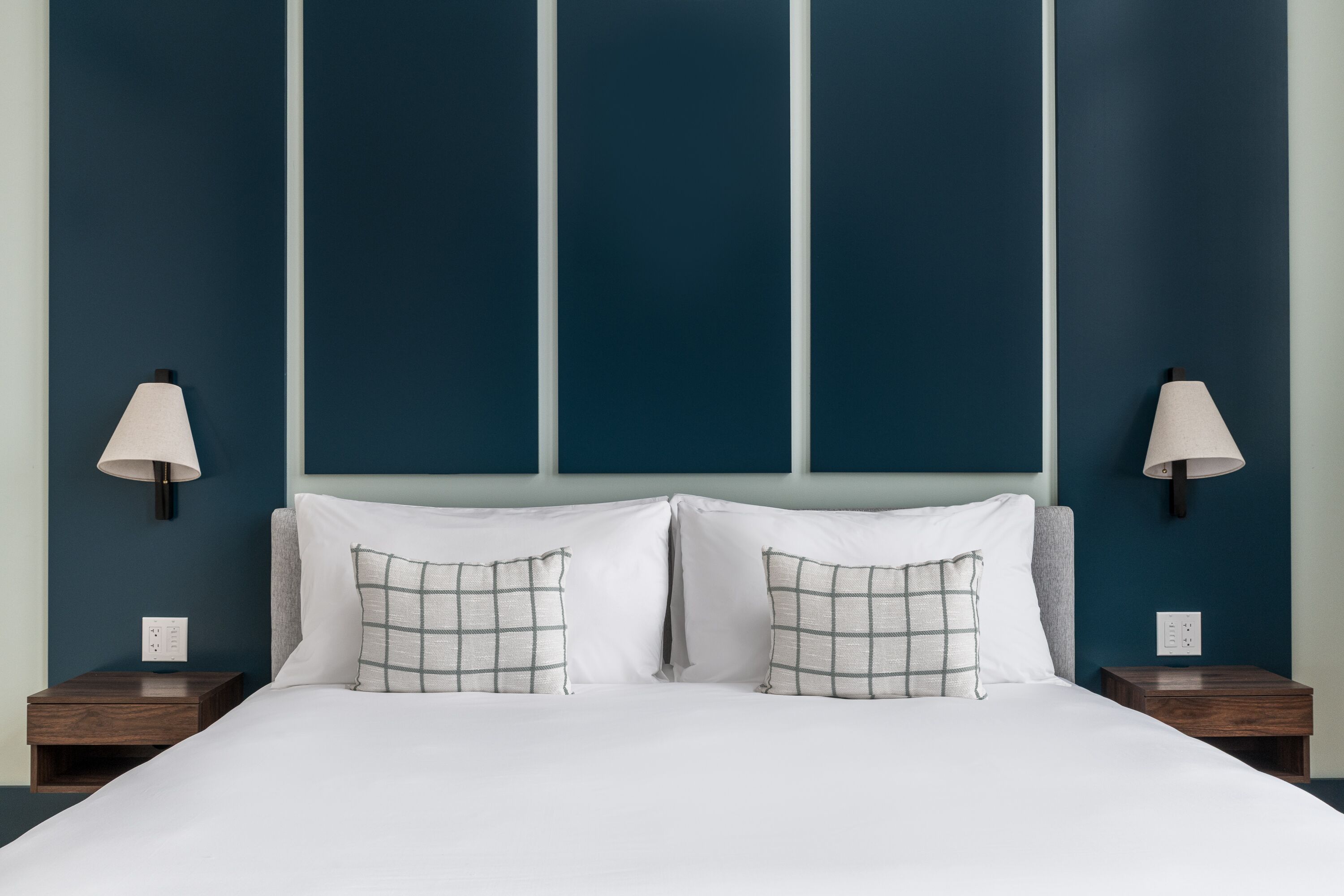 A neatly made bed with white linens and two pillows, flanked by two nightstands with lamps, against a wall with three vertical panels.