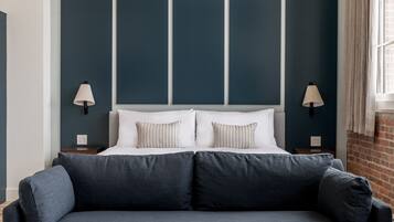Een moderne hotelkamer met een groot bed, twee bedlampen, een grijze bank en een bakstenen muur.