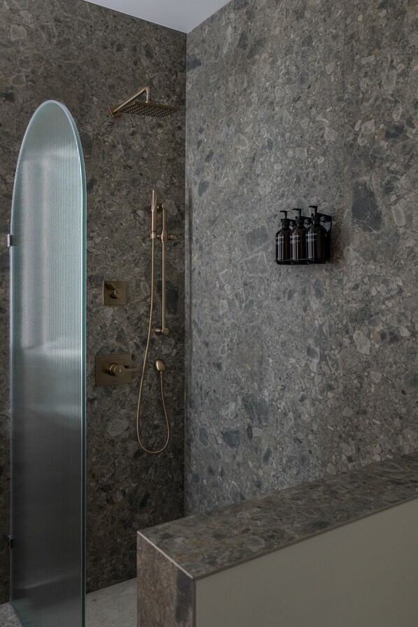 A modern bathroom with a glass shower enclosure, a handheld showerhead, and a wall-mounted faucet.