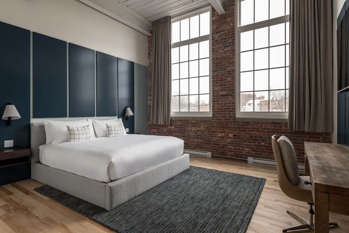 Habitación de hotel moderna con una cama grande, un escritorio y vistas de la ciudad a través de amplios ventanales.