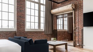 Una habitación moderna con pared de ladrillo, ventanas amplias, sofá, mesa y televisor.