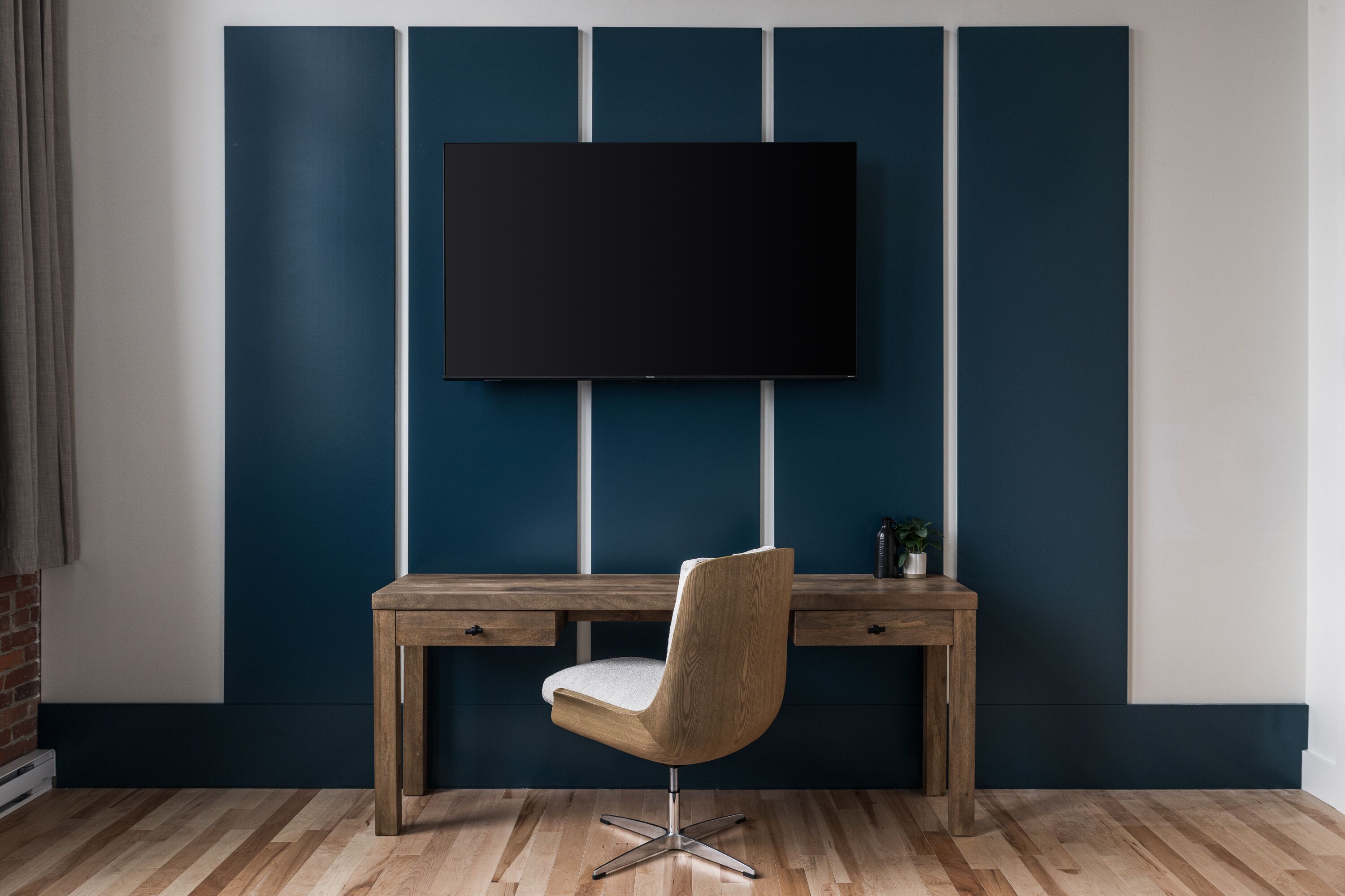 A modern room with a wooden desk, a chair, and a mounted TV.