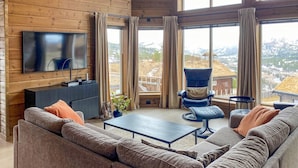 Un salon chaleureux avec un grand téléviseur, des sièges confortables et une vue sur un paysage enneigé.