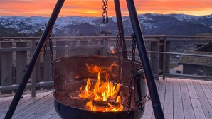 Un foyer suspendu sur une terrasse en bois, d’où l’on peut admirer des montagnes enneigées au coucher du soleil.