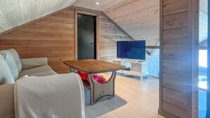 Une chambre à coucher confortable, aménagée en mezzanine, avec un plafond en bois, une table à manger en bois, un canapé et un téléviseur en arrière-plan.