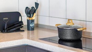 A kitchen with a black pot on an induction cooktop, a knife block, and a utensil holder. - The Sun by Stellar ALV (George Town)