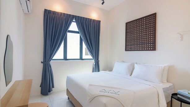 A hotel room with a bed, a desk, a chair, a window with curtains, and a wall-mounted air conditioner. - The Sun by Stellar ALV (George Town)