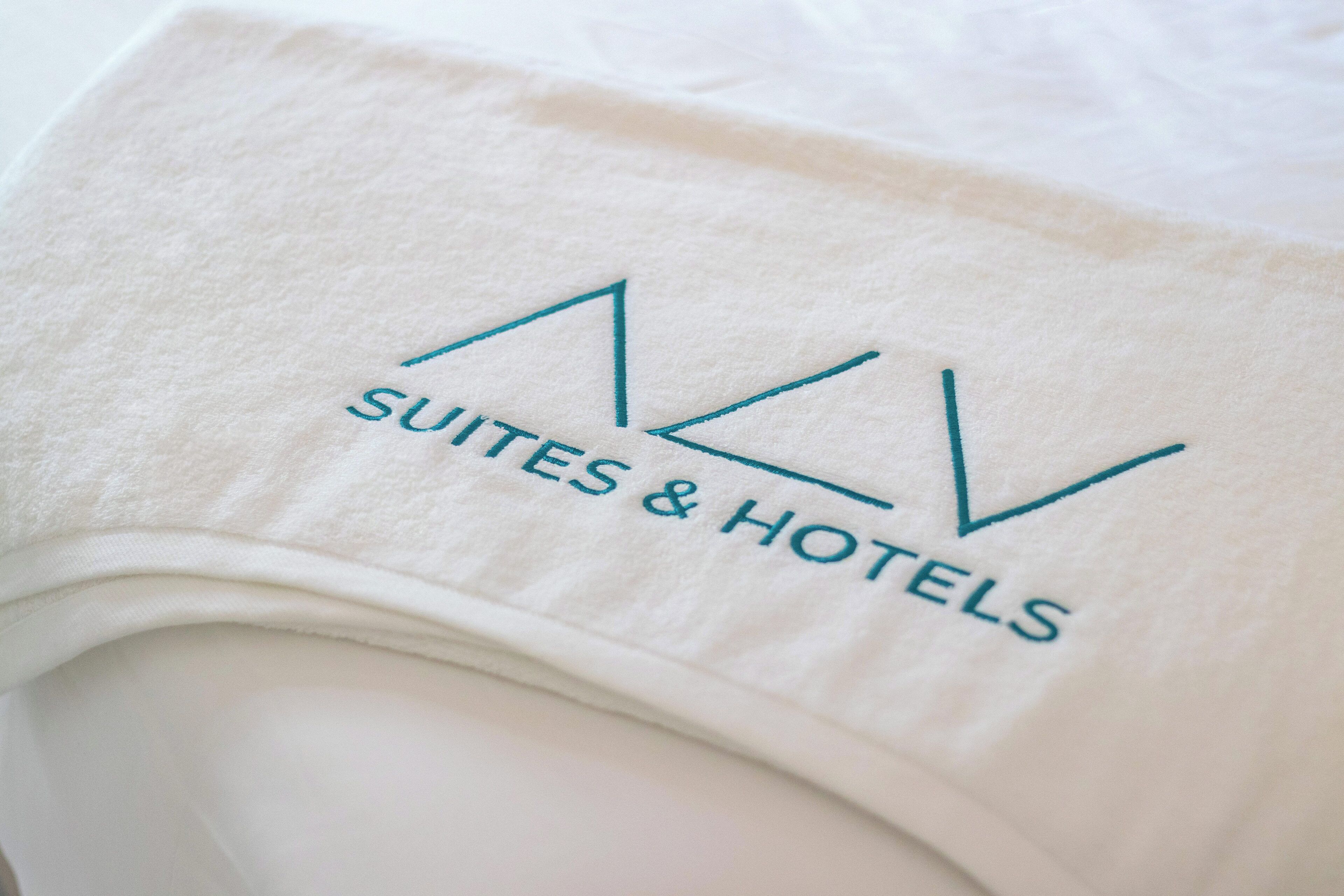A white towel with the logo and name "NV Suites & Hotels" embroidered on it.