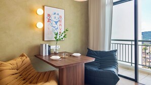 A modern living room with a wooden table, a sofa, a large window with a view, and a wall-mounted light fixture. - The Sun by Stellar ALV (George Town)