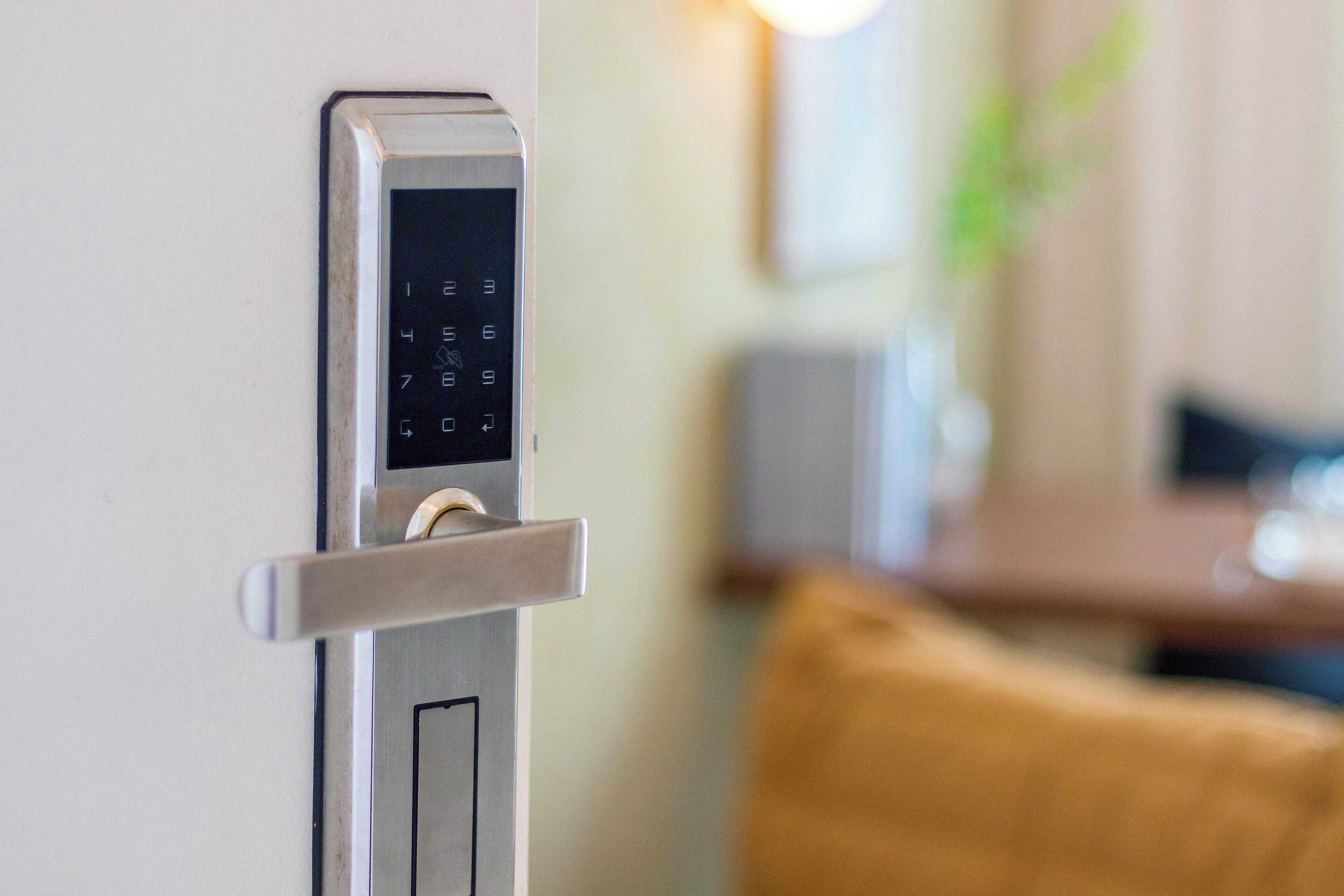Un tancament de porta metàl·lic modern amb teclat numèric, integrat en una habitació amb un fons borrat que inclou un sofà i una taula.