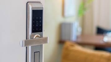 Un tancament de porta metàl·lic modern amb teclat numèric, integrat en una habitació amb un fons borrat que inclou un sofà i una taula.