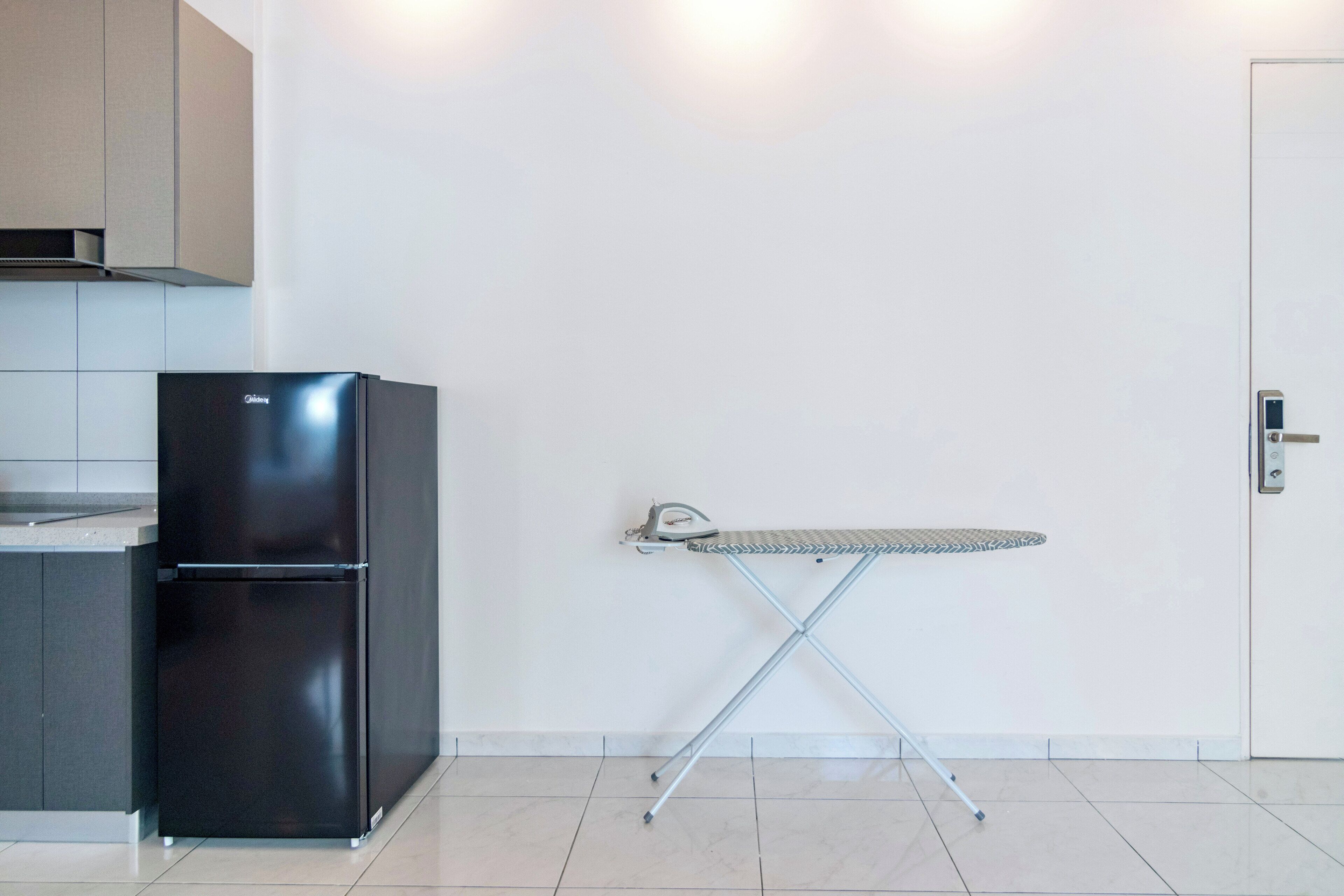 A compact kitchen with a black refrigerator, a small ironing board, and a white door.