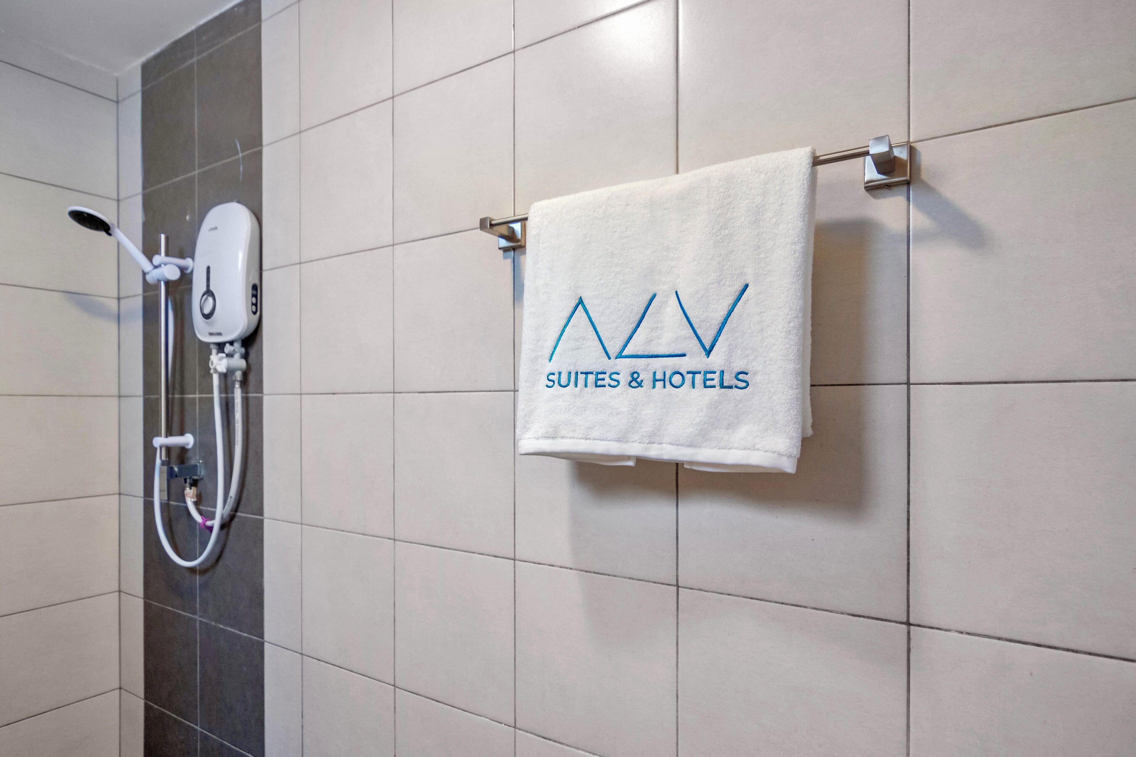 A bathroom with a towel rack holding a white towel with 'AV SUITES & HOTELS' embroidered in blue.