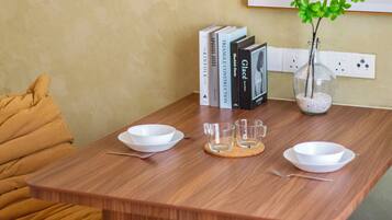 A wooden dining table with two white bowls, two clear glasses, and a small vase with green leaves.