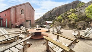 Un espace extérieur rustique aménagé avec des sièges, un foyer, des chaises en bois et un bâtiment rouge en arrière-plan.
