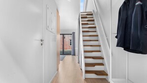 Un intérieur moderne avec un escalier en bois, des murs blancs et une étagère en métal.