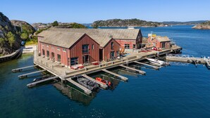 A waterfront building with multiple docked boats, a pier, and a clear view of the surrounding water and hills. - Awesome home in Søgne with WiFi (Søgne)