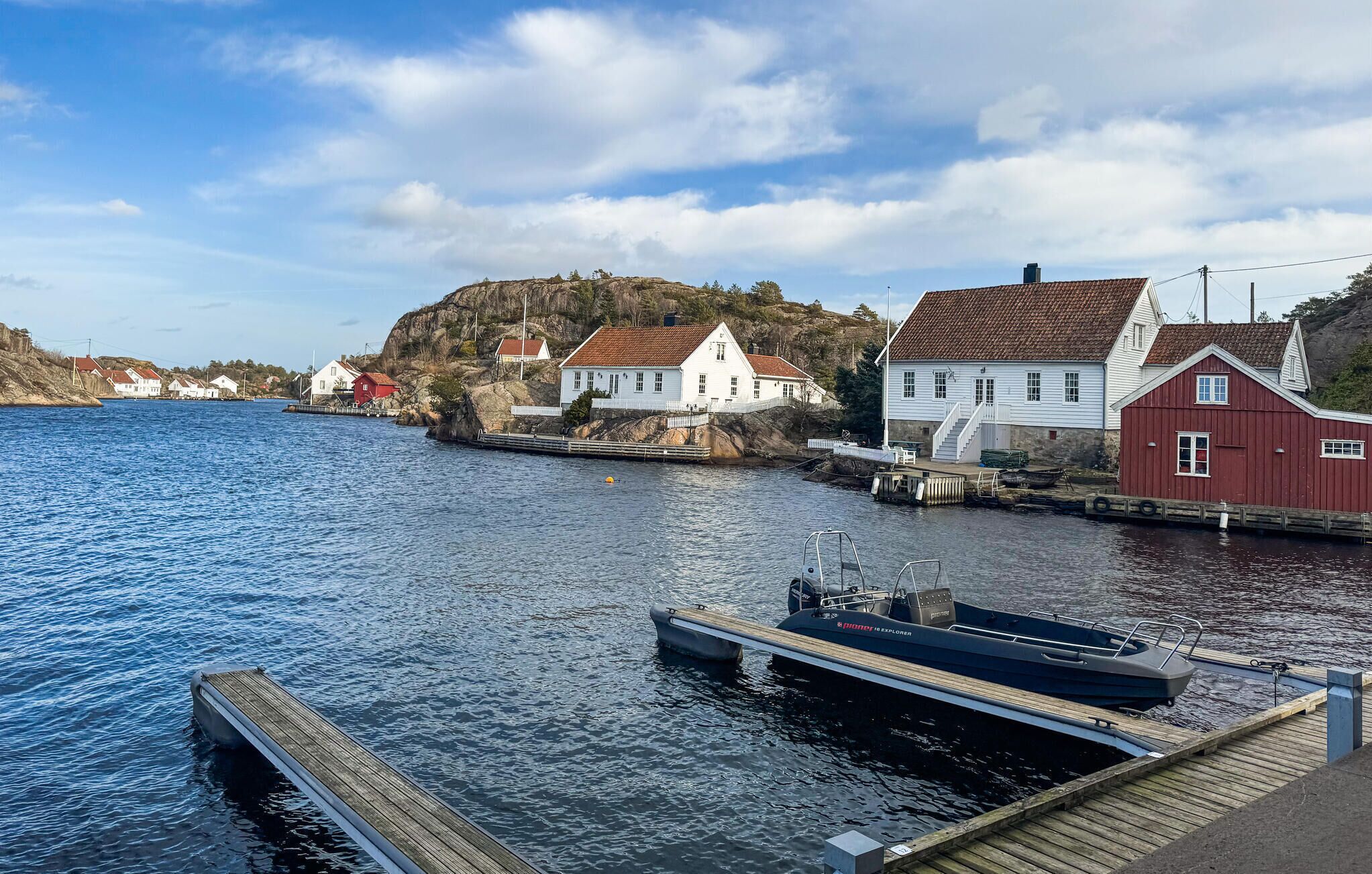 Ein Küstdorf mit weißen und roten Häusern, einem Steg und einem kleinen Boot.
