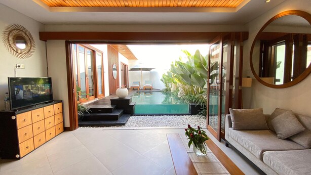 Ein modernes Wohnzimmer mit Fernseher, einer Couch und Blick auf einen Pool durch Glastüren.