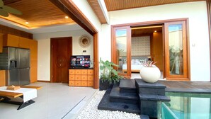 Ein modernes Wohnzimmer mit Fernseher, Holzausbau, einem Essbereich und Blick auf ein Schlafzimmer mit Bett und Wanddeko.