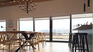 A modern interior with a wooden dining table and chairs, large windows with a view of a snowy landscape, and a bar area with stools. - Bakkar Luxuary Lodge (Grímsnes- og Grafningshreppur)