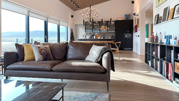 A modern living room with a leather sofa, a dining table, and a kitchen in the background. - Bakkar Luxuary Lodge (Grímsnes- og Grafningshreppur)