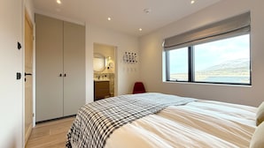 A bedroom with a large bed, a window with a view, a bathroom with a mirror and sink, and a closet. - Bakkar Luxuary Lodge (Grímsnes- og Grafningshreppur)