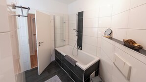 Une salle de bain moderne dotée d’une douche à parois de verre, d’une grande baignoire et d’un meuble-lavabo avec un miroir.