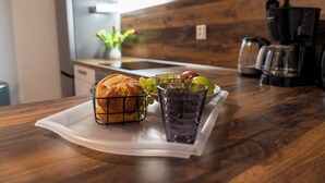 Un plateau de petit-déjeuner avec du pain, des raisins et un verre d’une boisson violette, posé sur un comptoir de cuisine en bois.