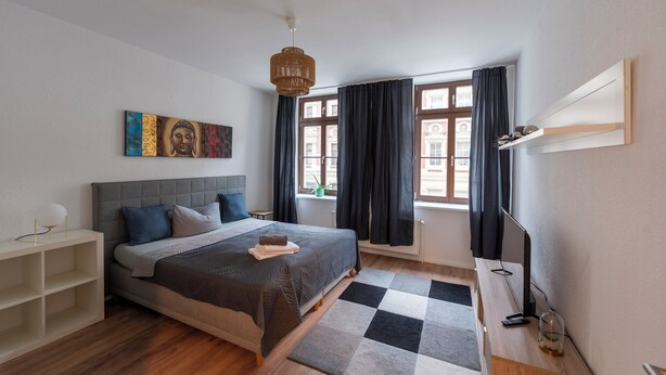Une chambre moderne avec un lit, une table de chevet, une lampe, une fenêtre avec des rideaux et une étagère fixée au mur.