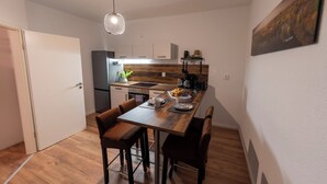 Une cuisine compacte dotée d’un plan de travail en bois, d’un four encastré et d’un réfrigérateur. On y trouve une table à manger avec quatre chaises et un luminaire suspendu.