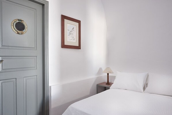 Un dormitorio con una cama, una mesita de noche con lámpara, un cuadro en la pared y una puerta con ventanal.