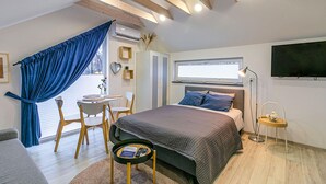Ein modernes Schlafzimmer mit Bett, Schreibtisch und Stuhl. Ein Fenster mit Jalousien, ein Deckenventilator und ein Flachbildfernseher an der Wand.