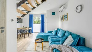 A modern living room with a blue sofa, a dining area with a wooden table and chairs, and a staircase with wooden beams. - Amazing home in Niechorze with sauna (Niechorze)