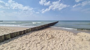 Une plage avec une jetée en bois qui s’avance dans la mer, un rivage sablonneux et un ciel dégagé.