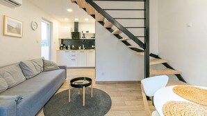Un espace de vie moderne comprenant un escalier, un canapé, une table basse et, au fond, un coin cuisine.